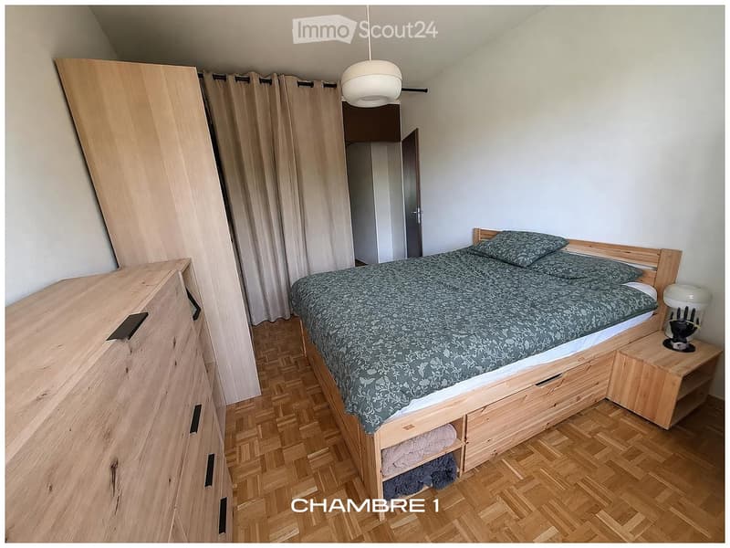 Bedroom with wooden bed, nightstand, wardrobe, and curtains. Wooden floor and white walls.