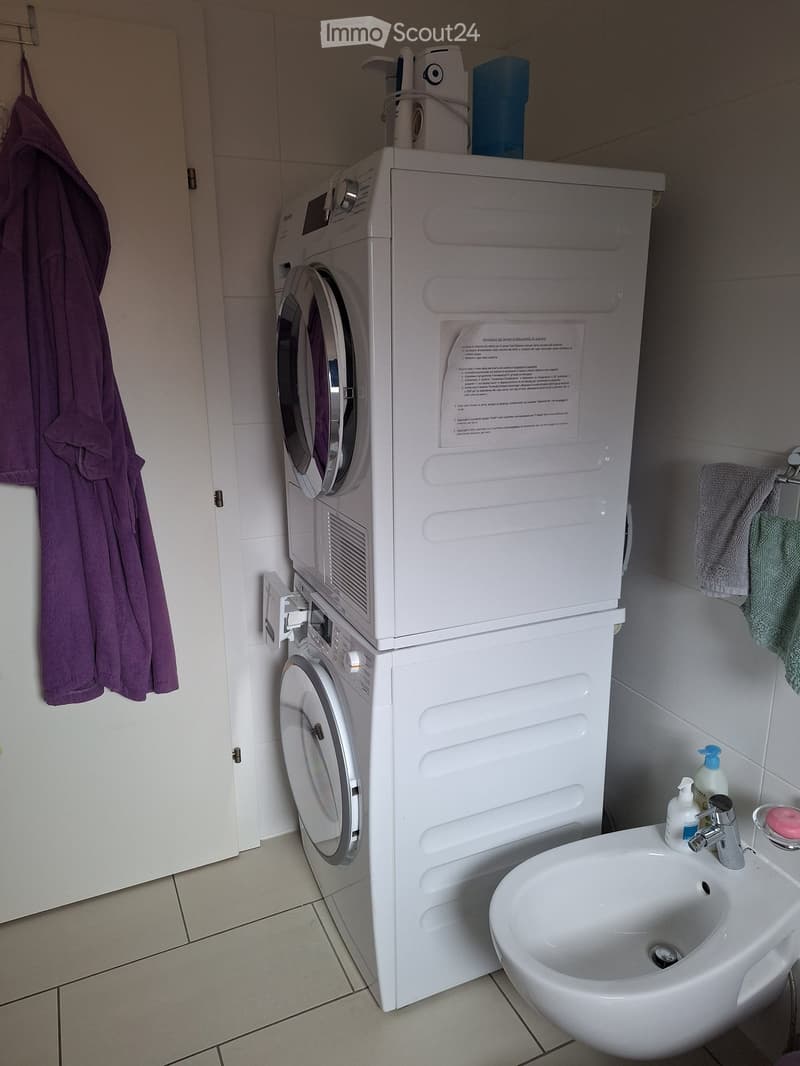 A compact bathroom with a white washing machine, a sink with a modern faucet, and a towel hanging on the wall.