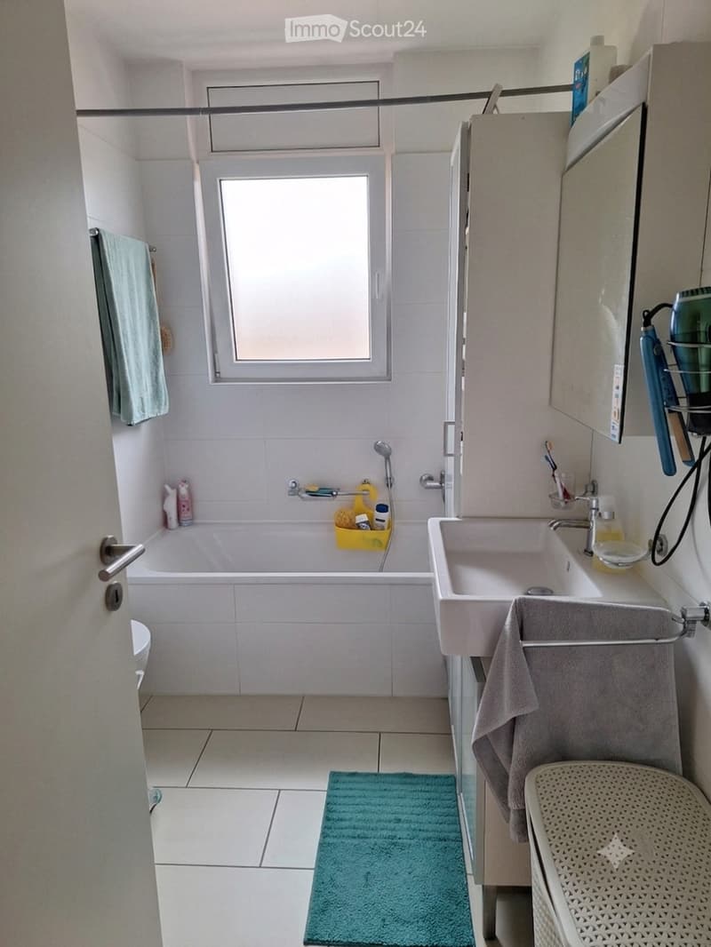 Modern bathroom with white tiles, a bathtub, a sink, a mirror, and a shower. Includes a towel, a small rug, and various bathroom accessories.
