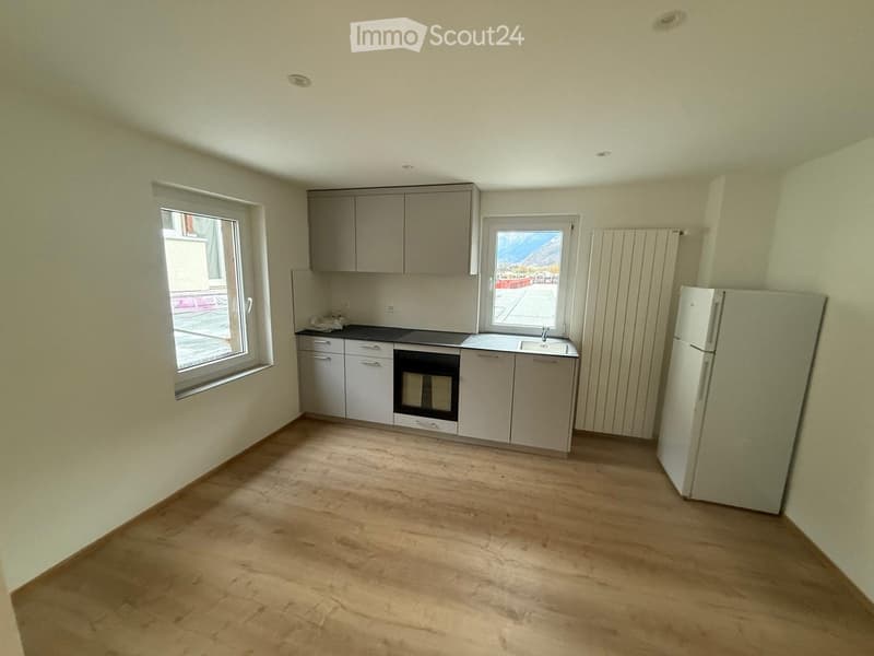 Open kitchen with wooden floors, white cabinets, black countertop, black oven, white refrigerator, and two windows