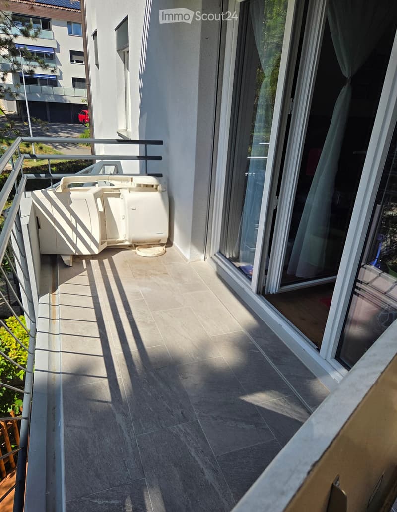 Balcony with tiled floor, metal railing, and a white storage unit. The balcony is adjacent to a sliding glass door leading into a room.