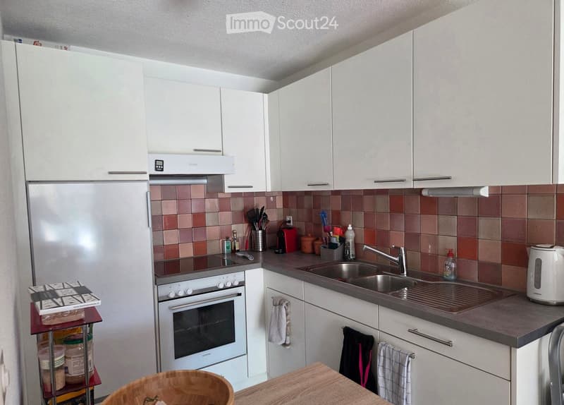 Modern kitchen with white cabinets, stainless steel appliances, and a dark countertop. Includes a refrigerator, oven, sink, and various kitchen utensils.