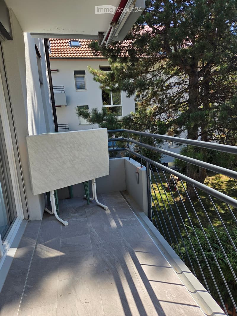 Balcony with tiled floor, metal railing, and a view of a neighboring building and trees.