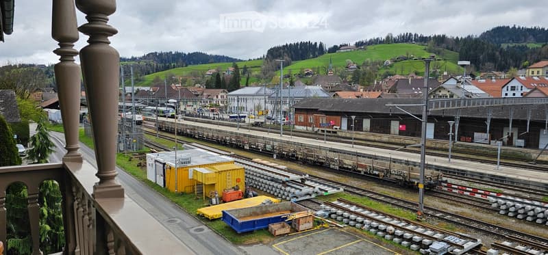View of a railway station with multiple tracks, buildings, and a mountainous background.
