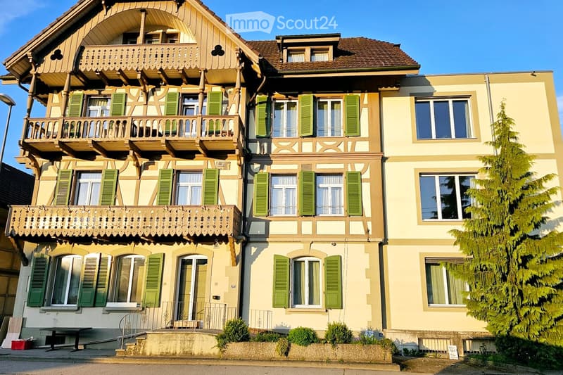 3 story house, yellow exterior, green shutters, balconies, front door, plants, tree