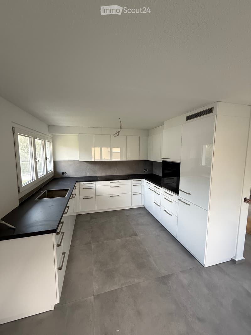 Modern kitchen with white cabinets, black countertops, and a sink, featuring large windows and a clean, minimalist design.