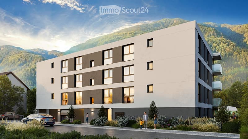 Modern multi-story residential building with balconies, large windows, and a view of the mountains. Features include a garage, parking area, and landscaped garden.