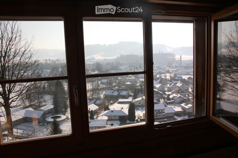 View from a room with large windows overlooking a snowy town and surrounding hills.