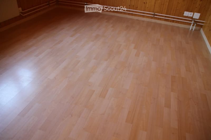 Empty room with light wooden flooring and wooden panel walls. No furniture or equipment present.