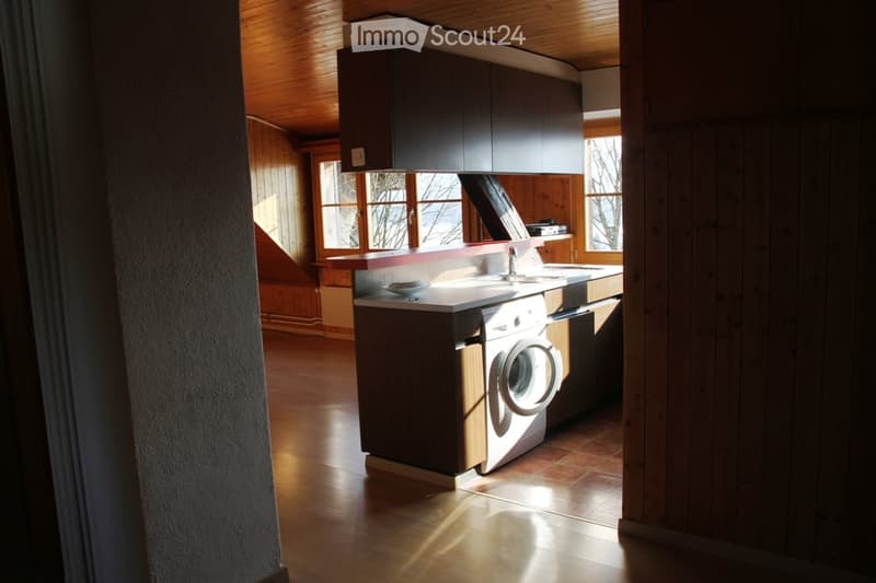 Modern kitchen with wooden cabinets, a sink, a washing machine, and a dishwasher, illuminated by natural light from large windows.