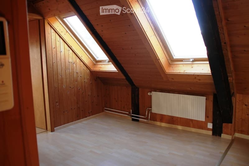 Empty attic room with wooden walls and floor, skylight windows, radiator, and exposed wooden beams.