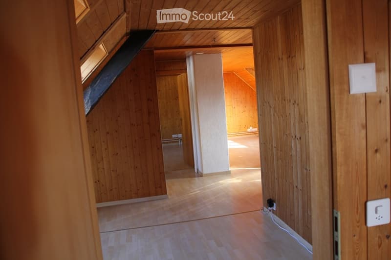 Empty wooden hallway with exposed beams, leading to another room. Natural light filters through a skylight at the far end.