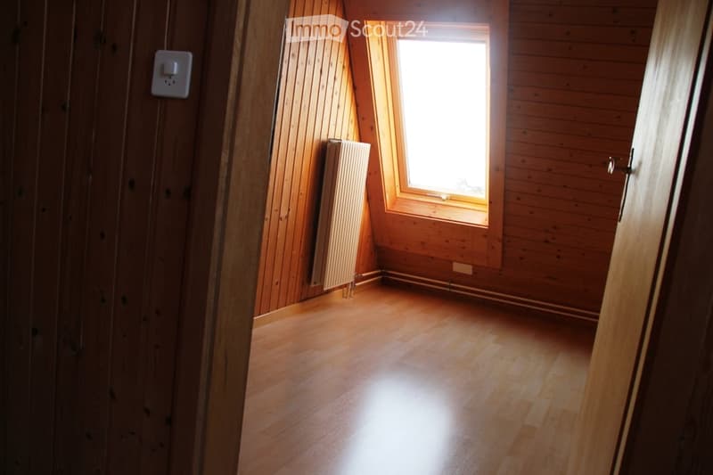 Empty room with wooden walls and floor, a single window, and a radiator. No furniture or equipment present.