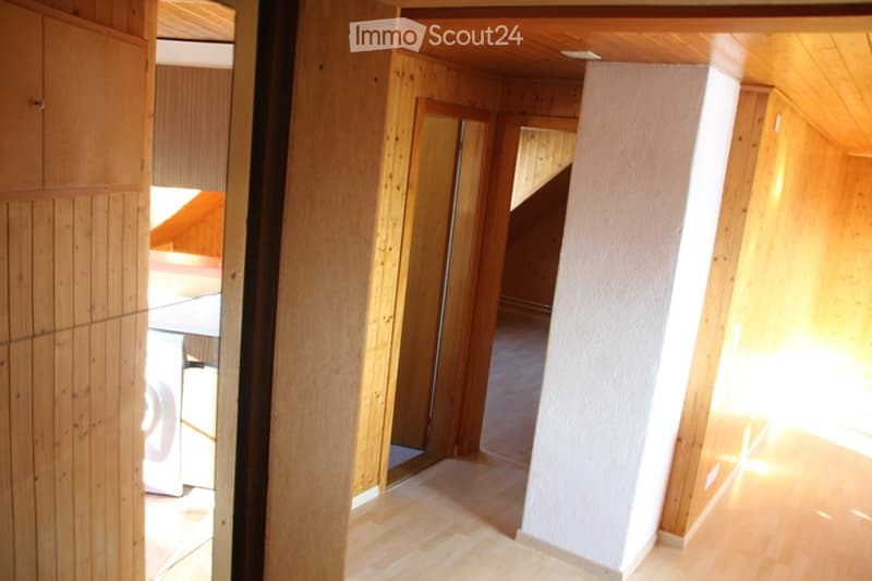 Bright, wooden-floored hallway with white walls, wooden doors, and a visible staircase leading upwards.