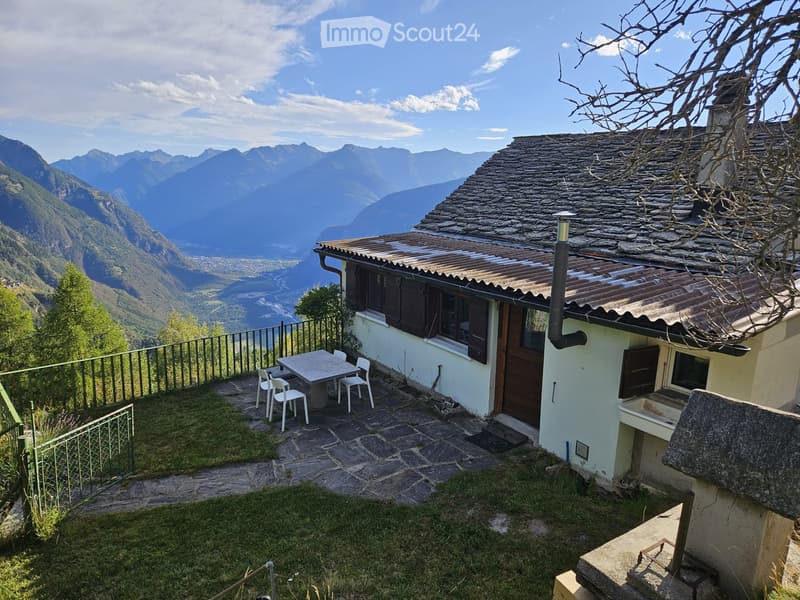 A small outdoor area with a table and chairs, overlooking a scenic mountain view.