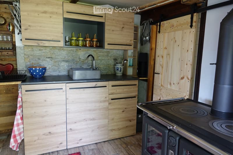 The kitchen features wooden cabinets, a stone backsplash, and a stainless steel sink. A stove with an oven is visible, along with various kitchen items such as jars, a bowl, and a towel.