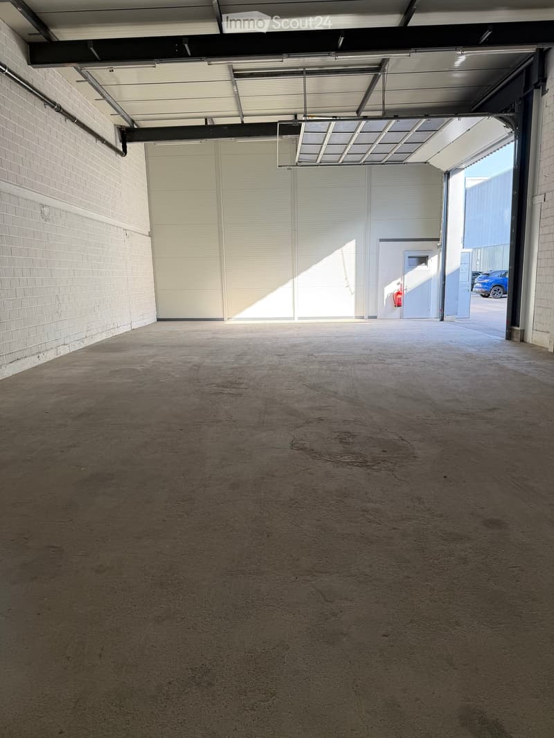 Empty garage with concrete floor, white brick walls, and a large overhead door leading to an outdoor area.