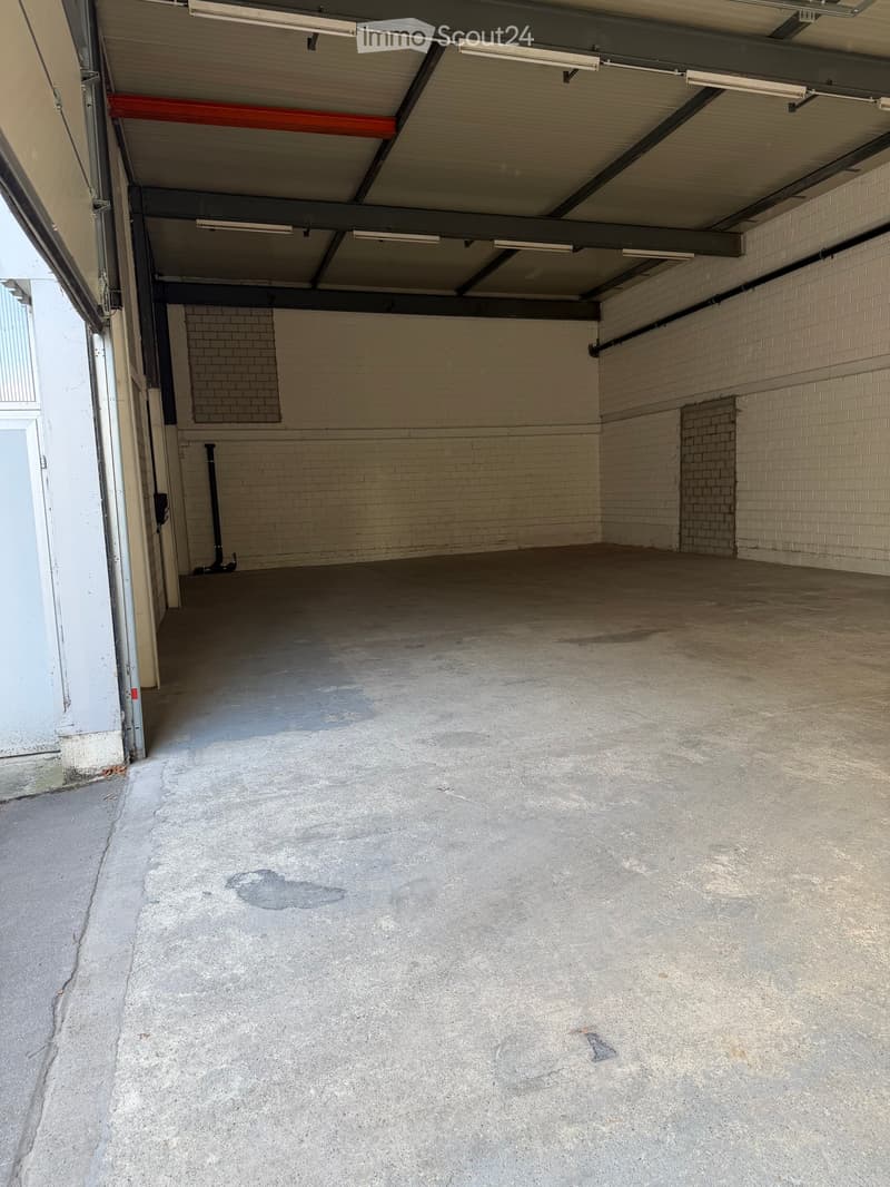 Empty garage with concrete floor, exposed brick walls, and metal ceiling beams.