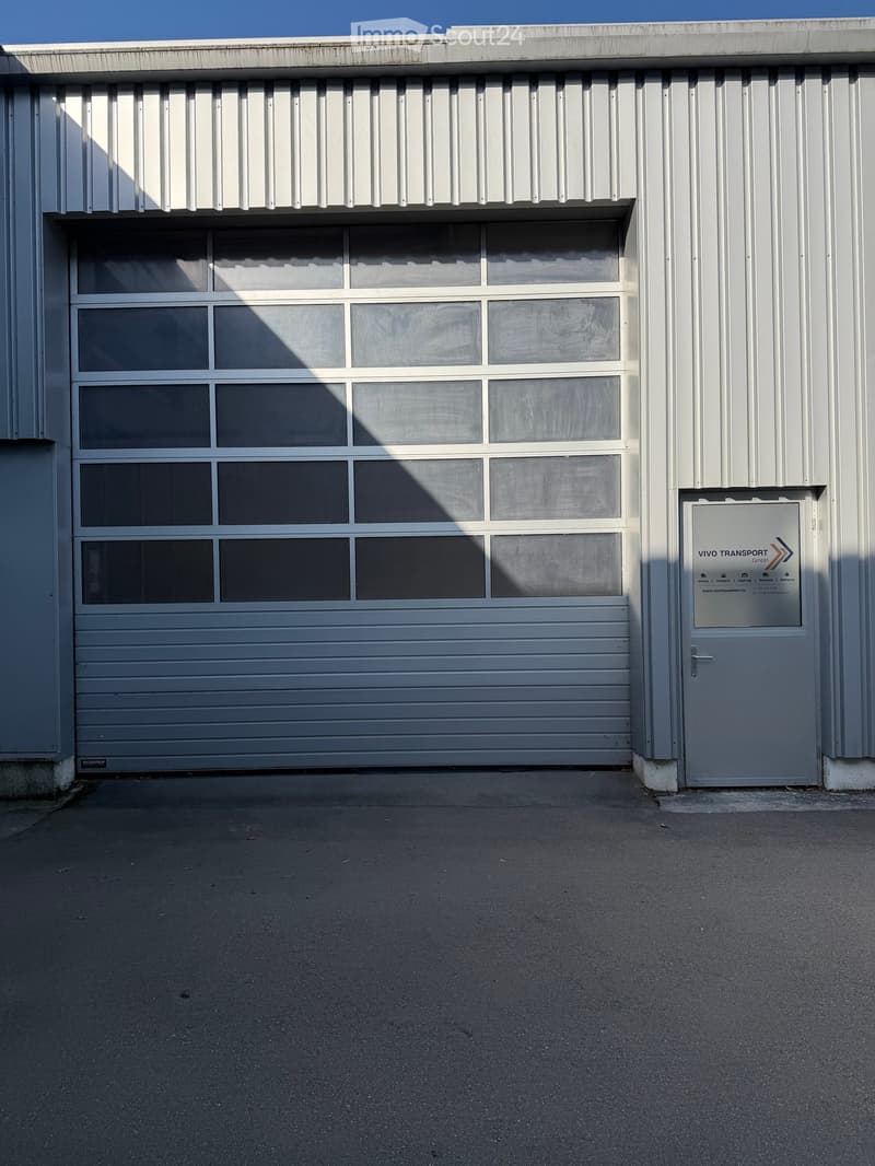 A large industrial-style building with a large garage door and a smaller side door, featuring a sign for "VIVO TRANSPORT GmbH".