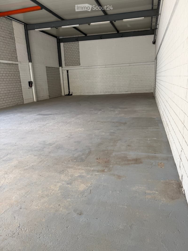 Empty concrete garage space with white brick walls, metal ceiling beams, and fluorescent lighting.