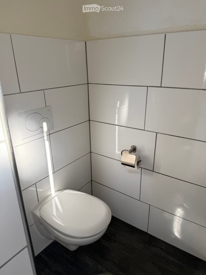 Modern bathroom with white tiled walls, a toilet, and a toilet paper holder mounted on the wall.