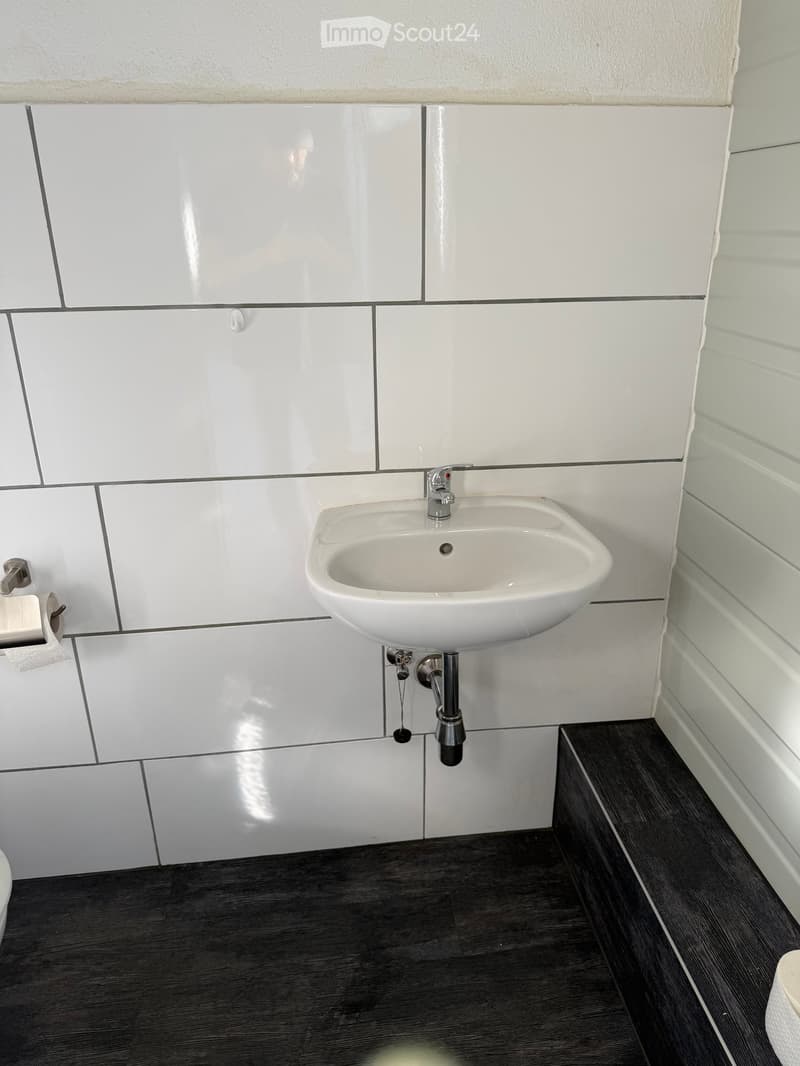 Modern bathroom with white tiled walls, a white sink with a chrome faucet, and a dark wooden floor.