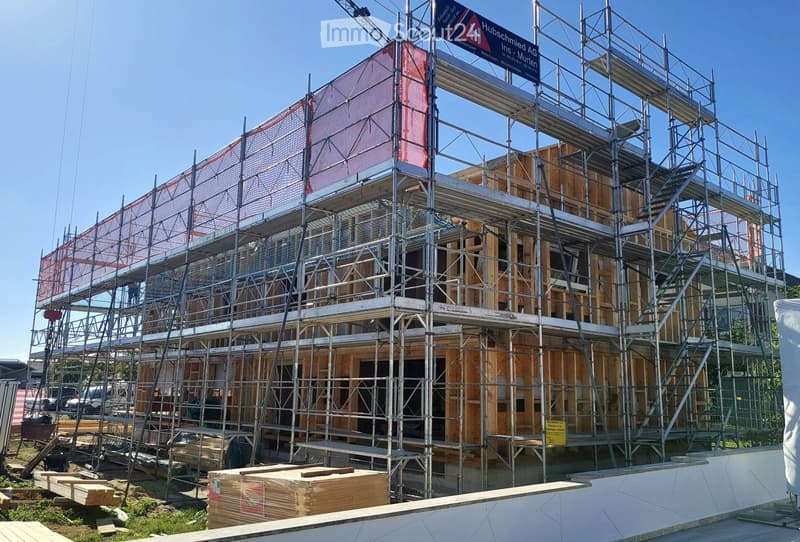 Multi-story building under construction with scaffolding, exposed wooden framing, and protective netting on upper levels.