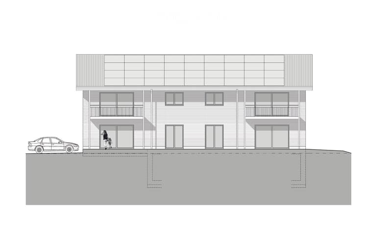 Two-story building with multiple windows and balconies, raised ground floor, and a parked car nearby.