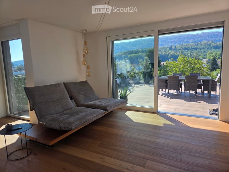 Modern living room with wooden flooring, large sliding glass doors leading to a balcony, grey sofa, small round table, and hanging pendant lights.