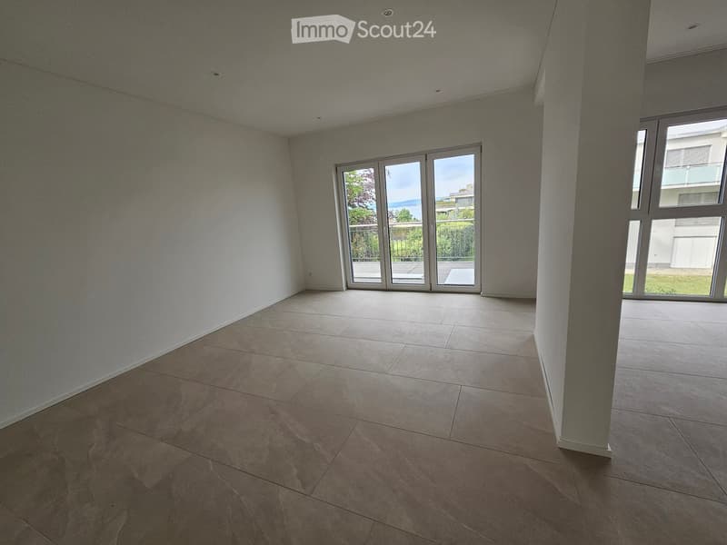 Empty room with tiled floor, white walls, large sliding glass doors leading to a balcony, and a window on the right side.