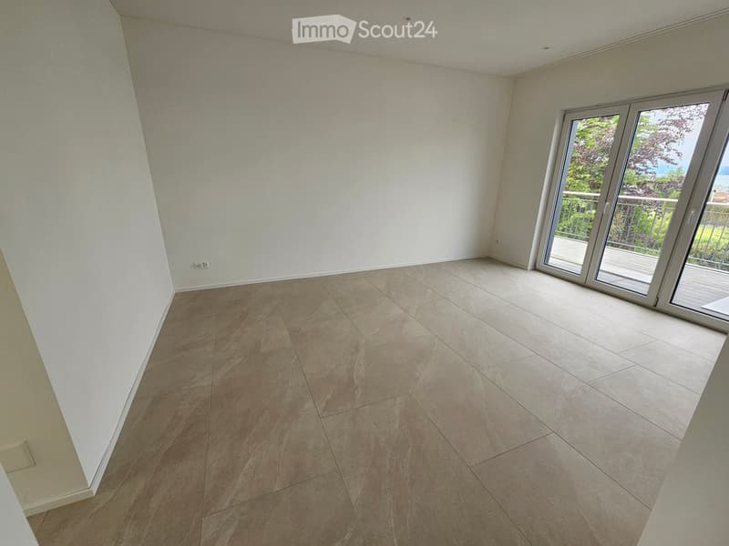 Empty room with light-colored tiled flooring and white walls, featuring a large sliding glass door leading to a balcony.