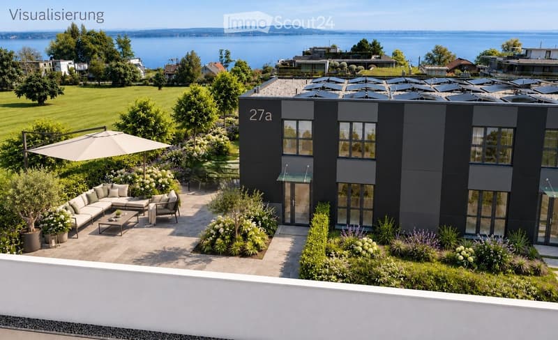 Modern outdoor patio area with a grey sofa, coffee table, chairs, umbrella, and lush greenery, overlooking a scenic lake view.