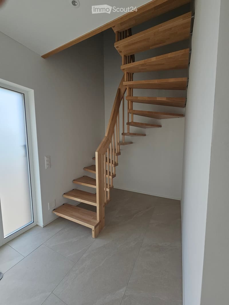 Spiral staircase with wooden steps and handrail, light grey walls, tiled floor, white door frame, and electrical outlet visible.