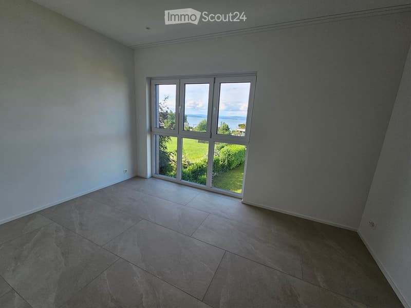 Empty room with tiled floor and large windows offering a view of a green lawn and water.