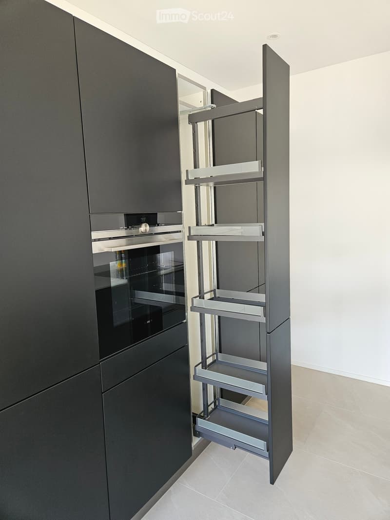 Modern kitchen with dark grey cabinets, a built-in oven, and an open shelving unit with multiple tiers.