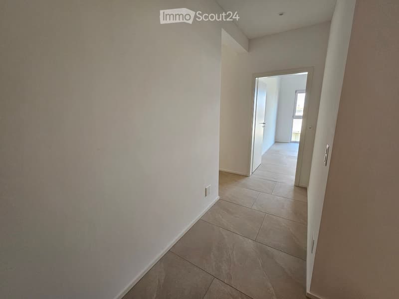 Empty hallway with tiled floor and white walls, leading to an open doorway.