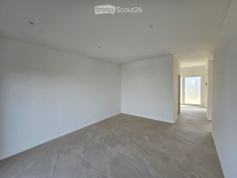 Empty room with white walls, grey tiled floor, and a doorway leading to another space.
