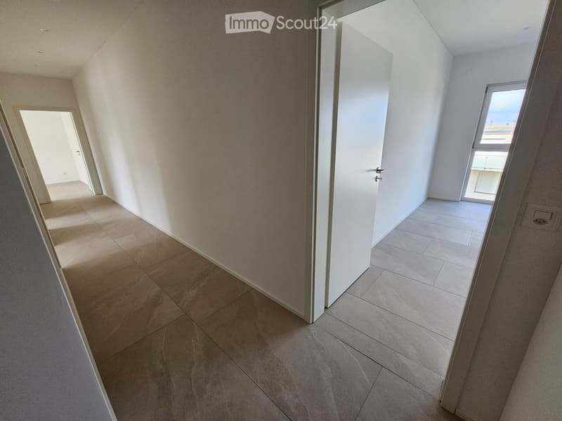 Empty hallway with tiled flooring and white walls, featuring two open doors leading to adjacent rooms.