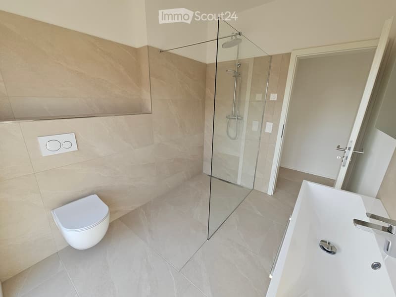 Modern bathroom with beige marble tiles, a white toilet, a bathtub, and a glass-enclosed shower area.
