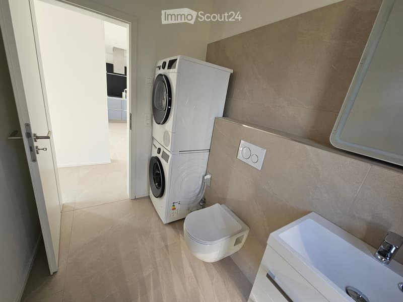 Modern bathroom with white tiles, a washing machine, toilet, and sink.