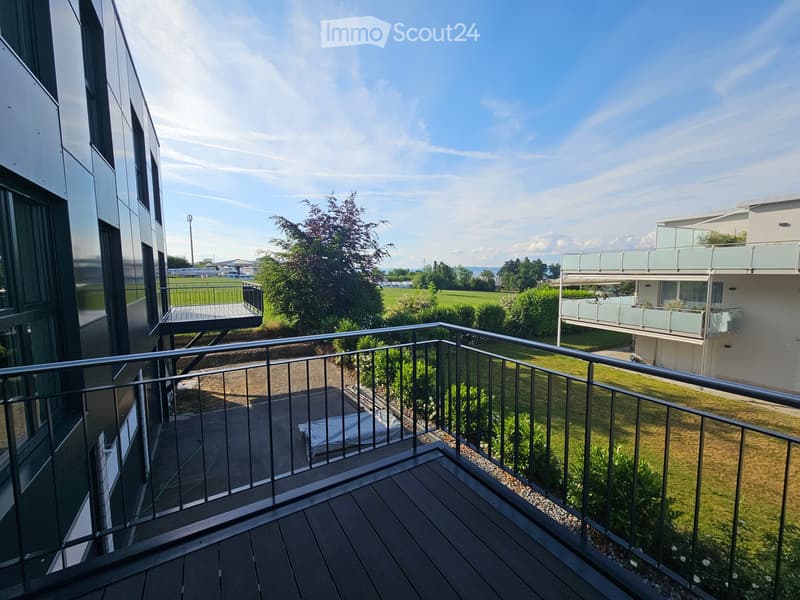Balcony with wooden decking, metal railing, and view of green lawn and neighboring building.