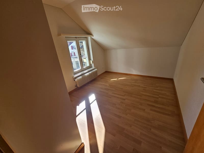 Empty attic room with wooden flooring, slanted ceilings, and a single window letting in natural light.