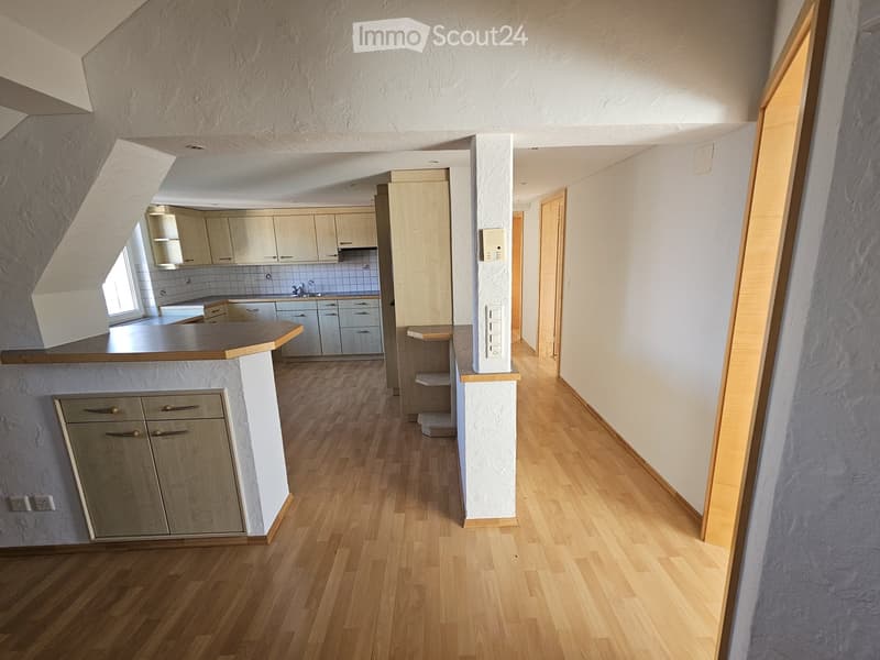 Empty hallway with wooden flooring, white walls, and a small kitchen area visible at the end.