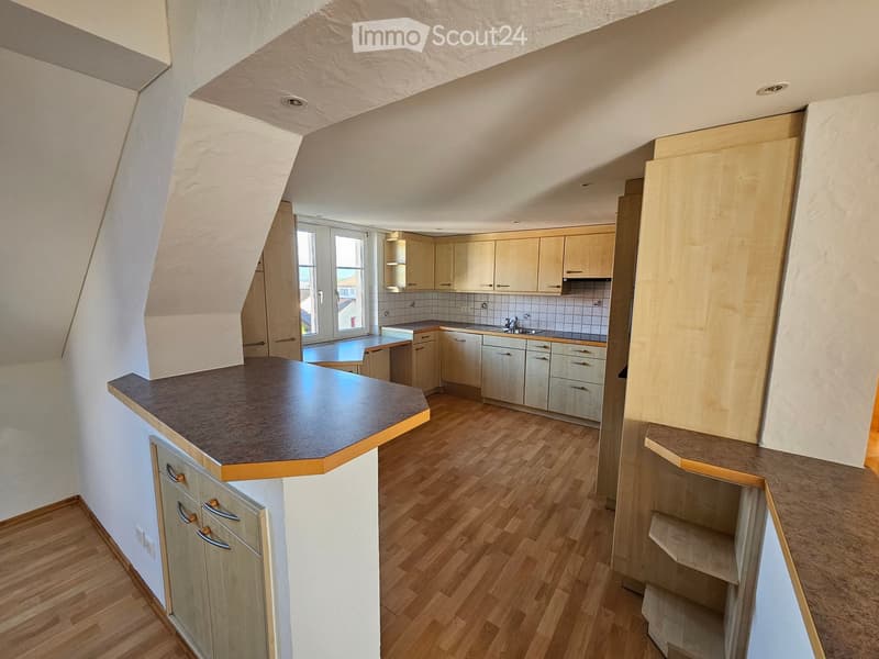 Modern kitchen with light wooden cabinets, a central island, and a sink area. The space features wooden flooring and large windows allowing natural light.