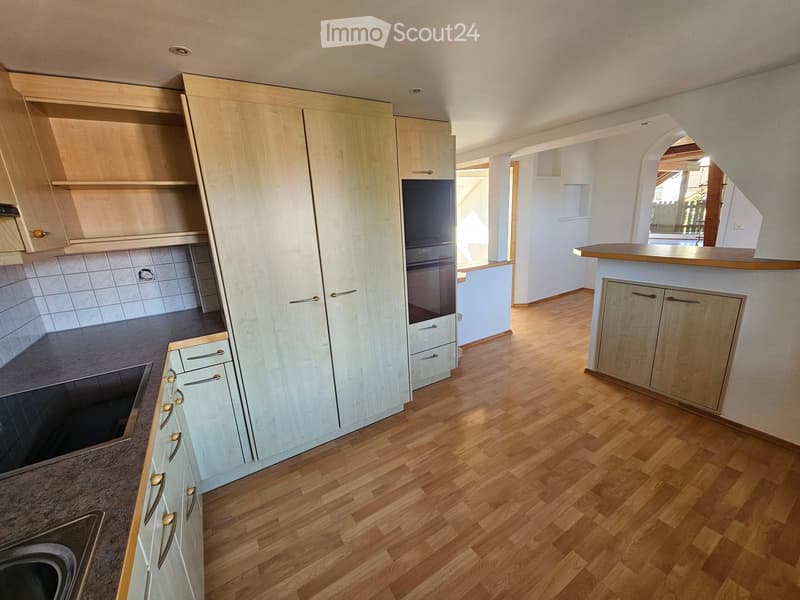 Modern kitchen with light wood cabinets, stainless steel appliances, and a wooden floor.