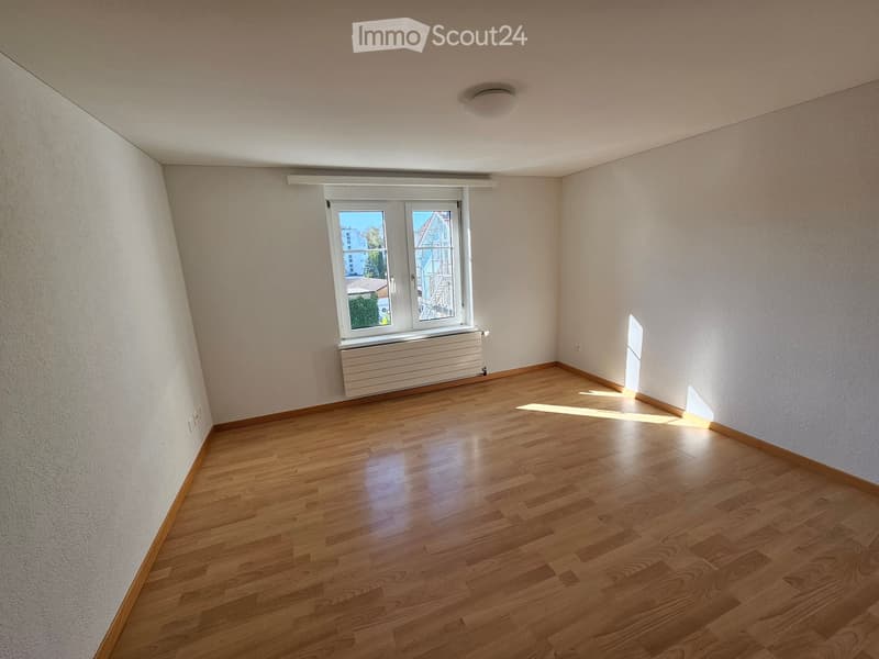 Empty room with wooden flooring, white walls, and a window with a radiator below it.