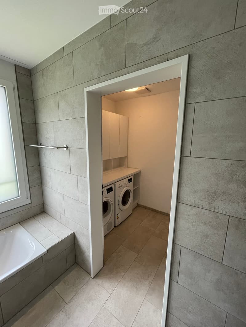 Modern bathroom with a bathtub, a washing machine, and built-in cabinets.