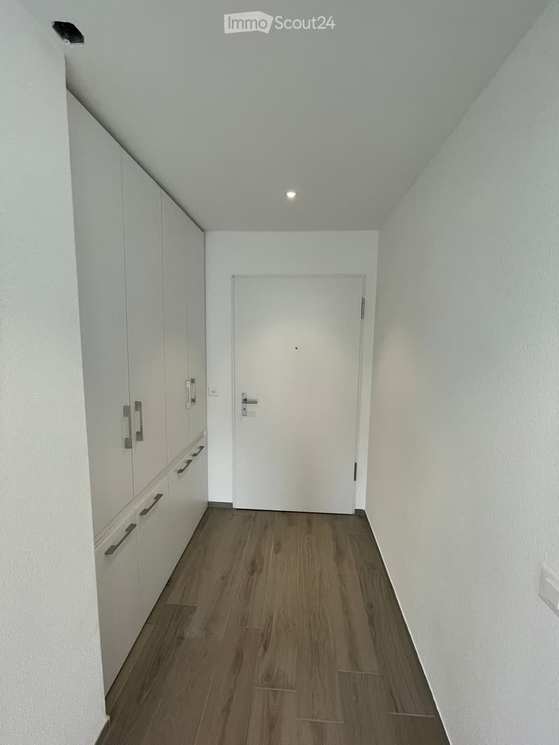Empty hallway with white walls, wooden flooring, and a white door at the end.