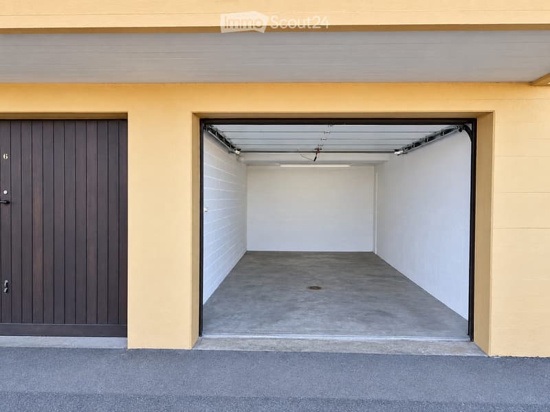 Empty garage with concrete floor, white walls, and a wooden door on the left.