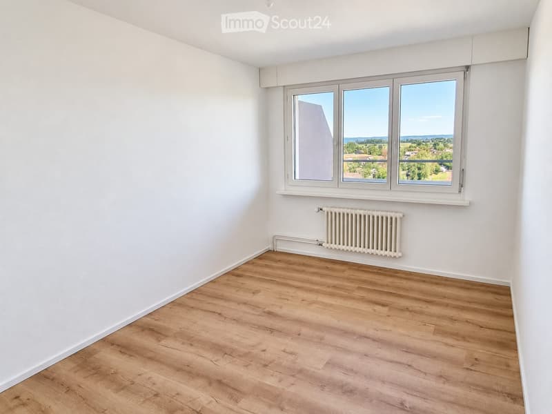 Empty room with light wooden flooring, white walls, and a large window offering a scenic view.